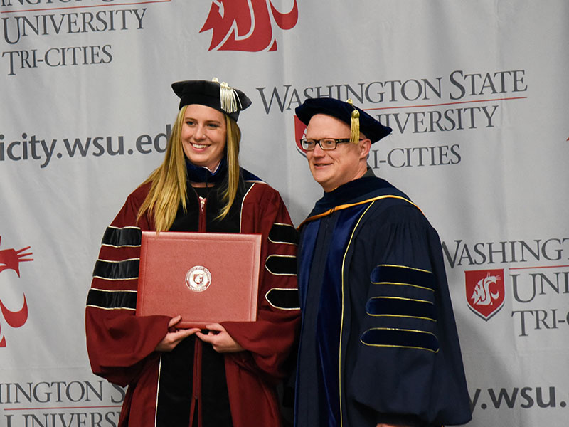 A graduate student receiving her diploma standing with professor